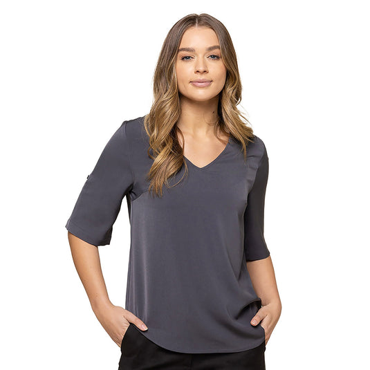 Reese V Neck Top showcased on a woman with hands in pockets, highlighting its elbow-length sleeves with tabs and a V neckline, crafted from luxe twill fabric for a stylish, professional look.