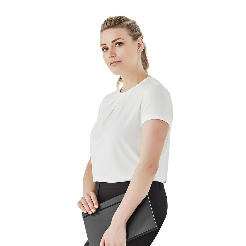 Load image into Gallery viewer, Biz Womens Blaise Short Sleeve Top: A woman in a white shirt holds a laptop. The semi-fitted design features a crew neckline and pleat details, offering stretch and comfort.