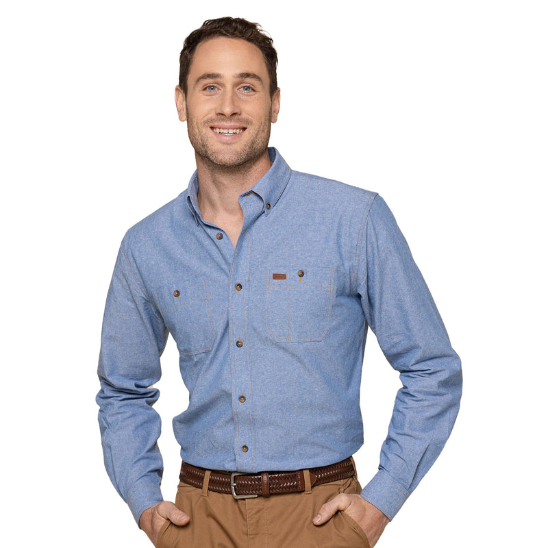 Load image into Gallery viewer, Icon Industrial Chambray Long Sleeve Shirt featuring a placket front, button-down collar, and double pockets. The shirt is worn by a smiling man with hands in pockets, showcasing its casual fit.