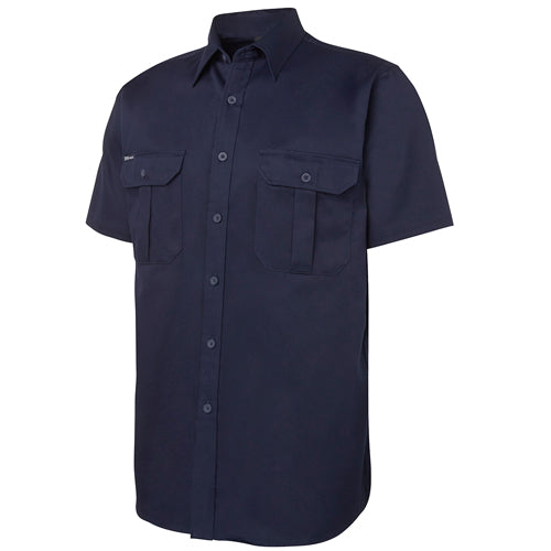 JB’s Classic Cotton S/S Work Shirt features short sleeves, a two-piece collar with a full button-down front, and two front pockets with button-down flaps and a pen insert for practical workwear.