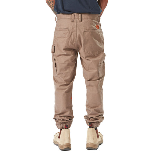 Volcom Workwear Caliper Cuffed Pant showcased with reinforced knees, tapered leg, and utility pockets, embodying durability and style, suitable for demanding work environments. Featured alongside tan boots for a complete workwear look.