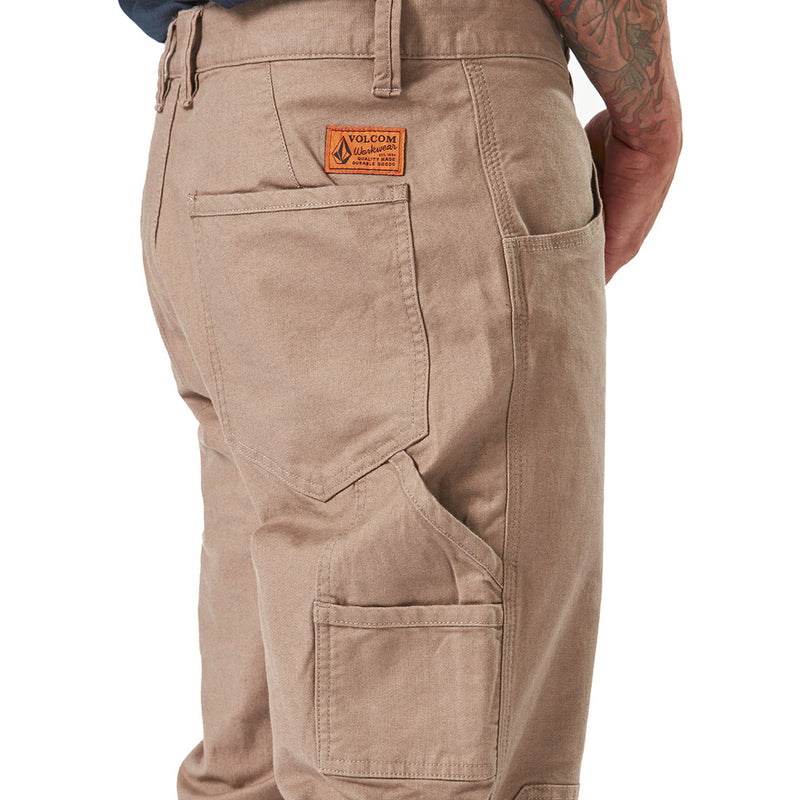 Load image into Gallery viewer, Volcom Workwear Caliper Cuffed Pant showcasing durable fabric, dual entry cargo pocket, and reinforced stitching, perfect for active safety work environments. The person's tattooed arm emphasizes the wearability and style.