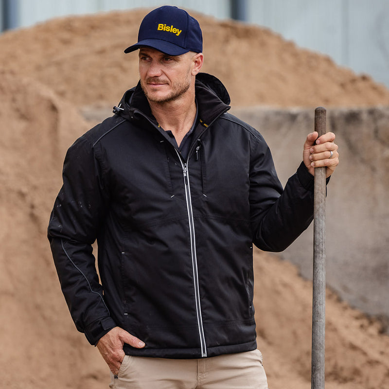 Load image into Gallery viewer, Bisley Heated Waterproof Hooded Jacket displayed as a man holds a shovel, showcasing its durable, waterproof fabric and adjustable hood, ideal for safety and work environments.