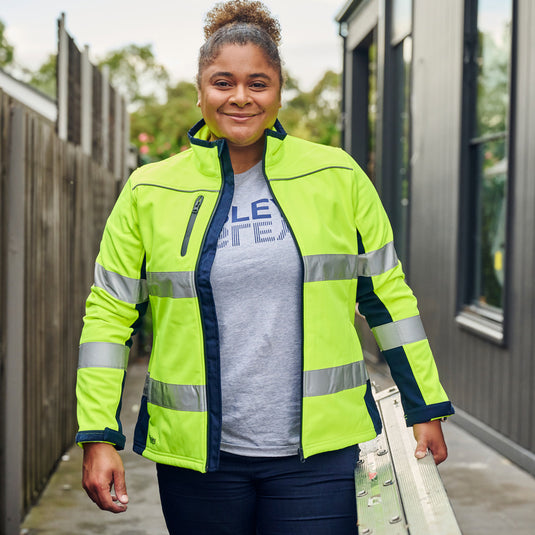 Bisley Women's Hi Vis Taped Soft Shell Jacket worn by a smiling woman, showcasing reflective taping on sleeves, showerproof fabric, and adjustable cuffs, embodying Active Safety's commitment to quality hi-vis clothing.