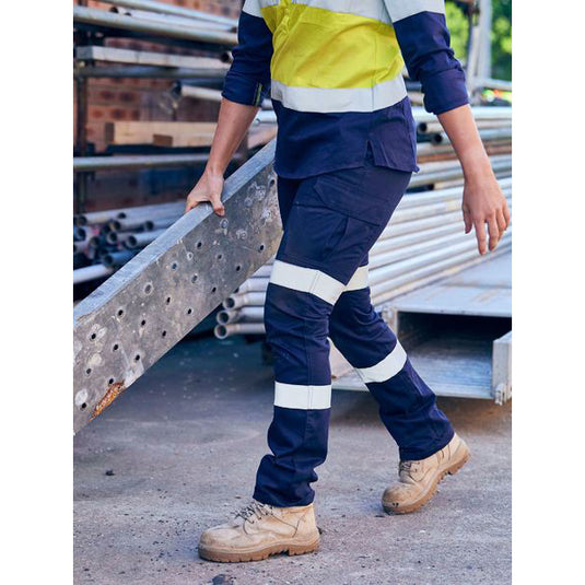 Bisley Women’s Taped Cotton Cargo Pants, Navy, worn by a person outdoors, feature a straight leg design, multiple pockets, and reflective tape, ideal for safety and comfort in active work environments.