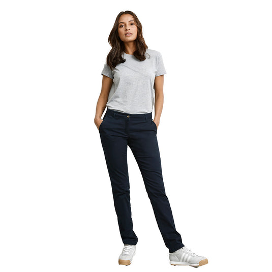 Biz Ladies Lawson Chino Pant worn by woman with hands in pockets; features slim, tapered leg and mid-rise fit, embodying casual workplace attire with a professional edge. Ideal for comfort and flexibility.