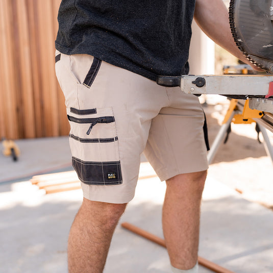 Bisley Flex & Move 4-Way Stretch Zip Cargo Short designed for durability with Cordura® reinforcement and multi-functional pockets, ideal for work environments. Modeled by a man holding a tool, showcasing flexibility.
