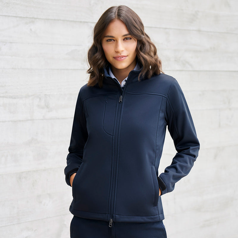 Load image into Gallery viewer, Biz Ladies Soft Shell Jacket with hands-in-pockets pose, featuring a two-way front zip, chin guard, stand-up collar, and zippered pockets, perfect for active safety in work environments.