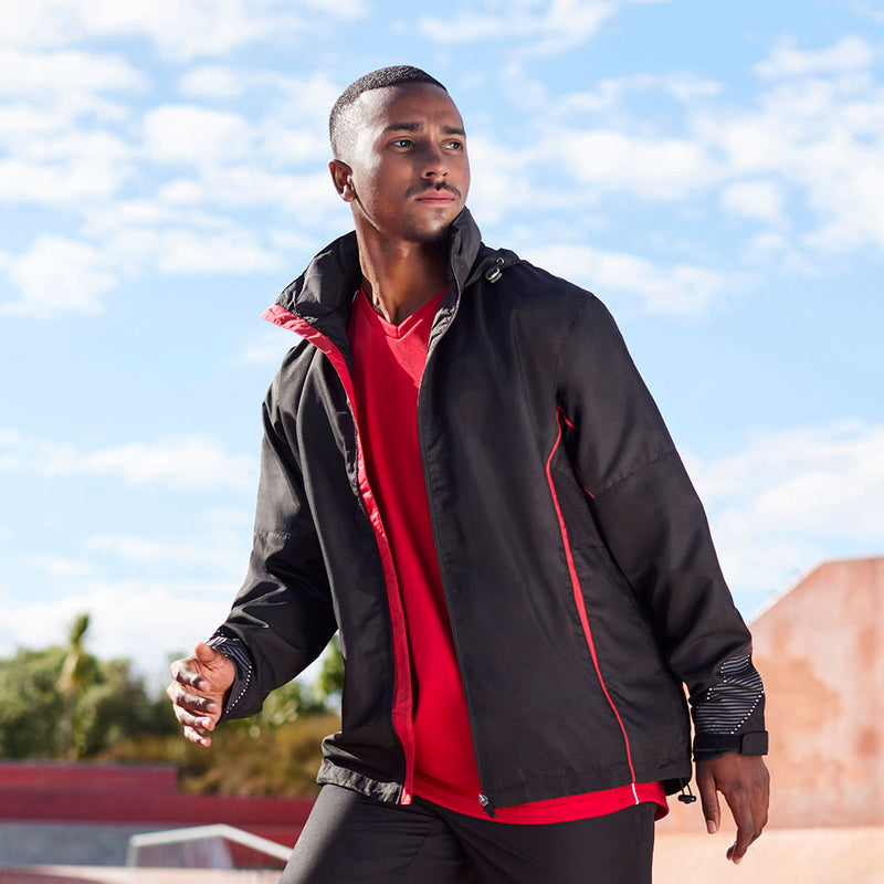 Load image into Gallery viewer, A young man in motion wears the Biz Adults Razor Team Jacket, featuring reflective trims and a stowaway hood, ideal for active comfort in a skate park setting.