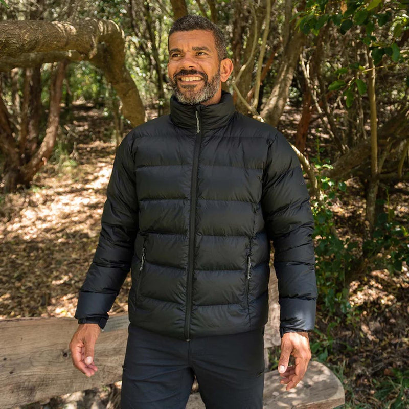 Load image into Gallery viewer, Man outdoors wearing Macpac Adult Halo Down Jacket, Black, showcasing its quilted design, adjustable cuffs, and warmth-retaining features, ideal for safety and comfort in cool environments.