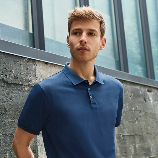 Biz Mens City Short Sleeve Polo featuring a waffle knit collar and pearlized buttons, modeled by a man standing outdoors, showcasing its breathable cotton and elastane stretch fabric.