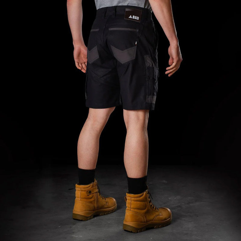 Load image into Gallery viewer, Man wearing BAD Attitude Slim Fit Work Shorts with reinforced pockets and a smartphone pocket, paired with brown boots, showcasing workwear functionality and style.