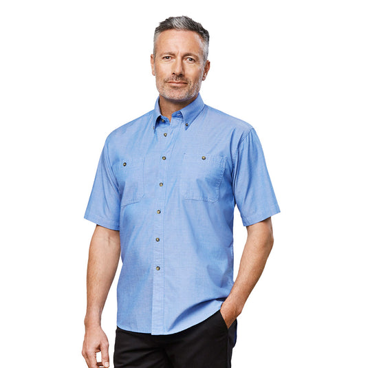 Biz Chambray Short Sleeve Shirt, featuring a button-down collar and chest pockets, is shown on a man. This workwear staple highlights its wrinkle-resistant fabric and traditional fit, ideal for workplace environments.