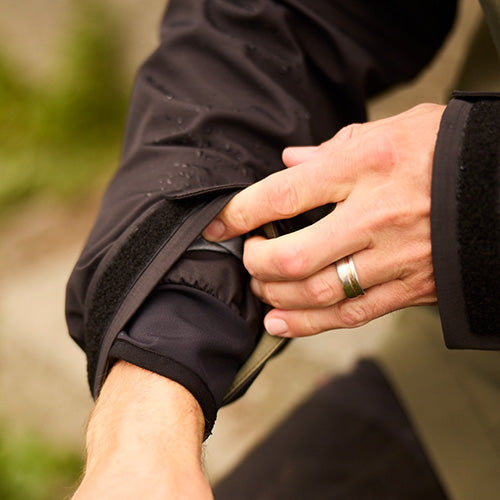 Load image into Gallery viewer, The Line 7 Territory Storm Pro20 Waterproof Jacket, shown with hands adjusting its Velcro cuff closures, features durable waterproof fabric, reflective branding, and large zipped pockets, ideal for outdoor safety and work environments.