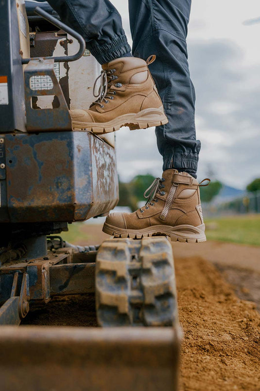 A person climbing onto a piece of machinery, wearing a pair of wheat zip side Blundstone Safety Boots. The work boots are part of Active Safety's Safety Footwear range.