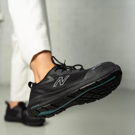 A close up of a New Balance Safety Shoe being worn indoors. The safety shoe looks breathable with side mesh and durable with toe protection and a solid sole.