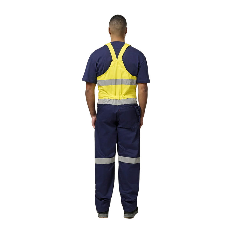 Load image into Gallery viewer, The Hard Yakka Easy Action Hi Vis Cotton Bib Overall showcases a back view, featuring a high-visibility yellow vest, reflective strips, and navy workwear, highlighting its practical design for workplace safety.