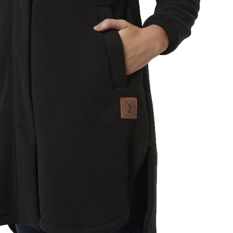 Load image into Gallery viewer, Hard Yakka Womens Longline Zip Hoodie, Black, showcasing a person wearing the hoodie with a close-up of the sleeve and hand, highlighting its longline fit and practical design features.