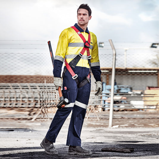 Syzmik Rugged Cooling Taped Overall: A person in safety gear holding a tool, showcasing the overall's reinforced stress points, reflective tape, and convenient pockets, ideal for active workplace safety and durability.