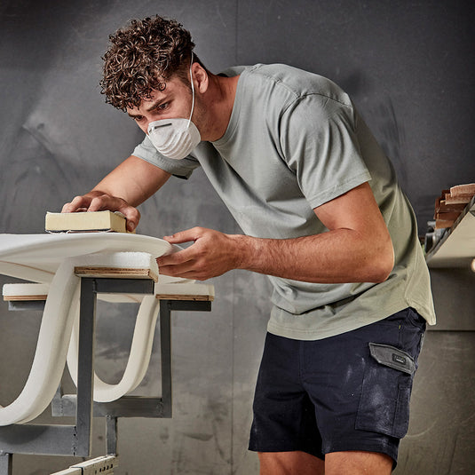Syzmik Streetworx T-Shirt worn by a man with a mask, featuring a modern slim fit and longer tail with curved hem. The lightweight, breathable cotton fabric is perfect for active environments.