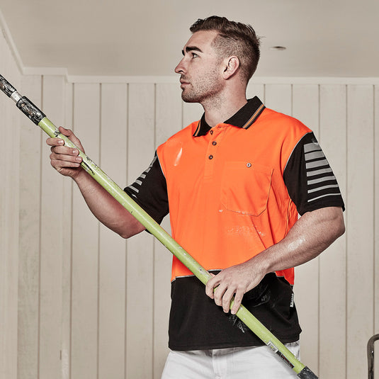 Syzmik Hi Vis Zone Polo Shirt: A man holds a paintbrush, wearing a moisture-wicking, breathable polo shirt featuring sleeve print and 3M™ reflective details, ideal for active safety environments.