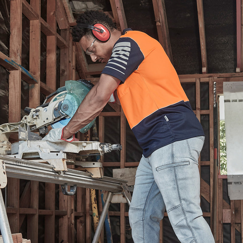 Load image into Gallery viewer, Syzmik Hi Vis Zone Polo Shirt worn by a man using a circular saw, featuring 3M™ reflective piping and sleeve print design, ideal for safety and visibility in construction environments.