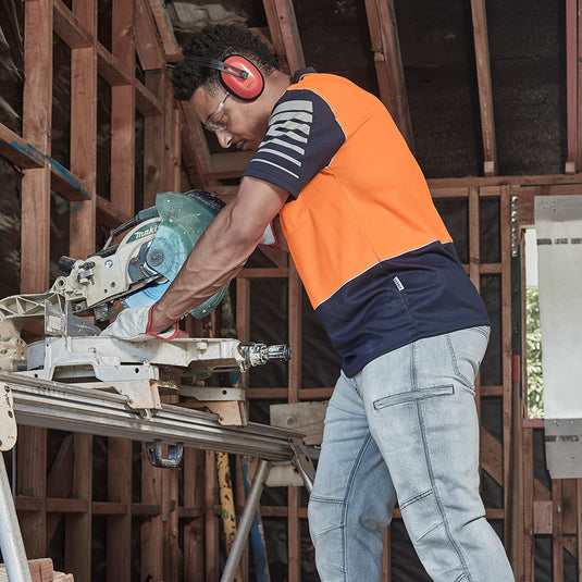 Syzmik Hi Vis Zone Polo Shirt worn by a man using a circular saw, featuring 3M™ reflective piping and sleeve print design, ideal for safety and visibility in construction environments.