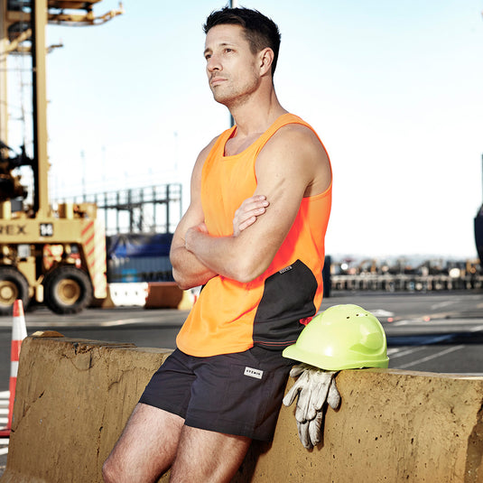 Syzmik Hi Vis Squad Singlet featured on a man leaning against a concrete wall, showcasing its breathable, moisture-wicking design with contrast side panels, ideal for safety and active environments.