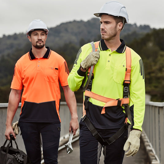 Syzmik Flux Hi Vis L/S Polo Shirt worn by men in safety gear, featuring a breathable mesh side panel and chest pocket, ideal for hot conditions and workplace safety.