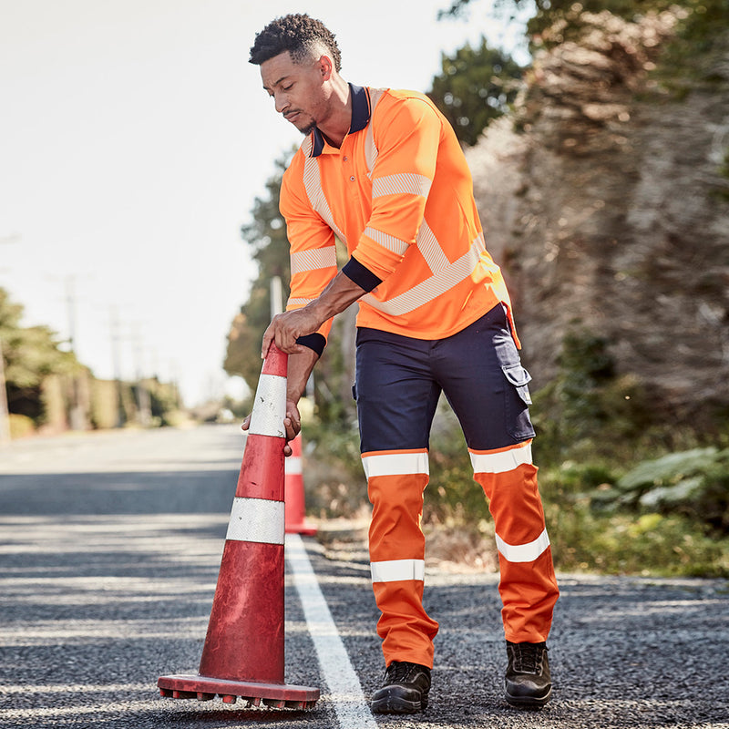 Load image into Gallery viewer, Syzmik Hi Vis TTMC-W Segmented Tape Polo Shirt worn by a man, depicted outdoors holding a traffic cone, showcasing its breathable polyester fabric and flexible, ultra-comfortable design suitable for safety work environments.