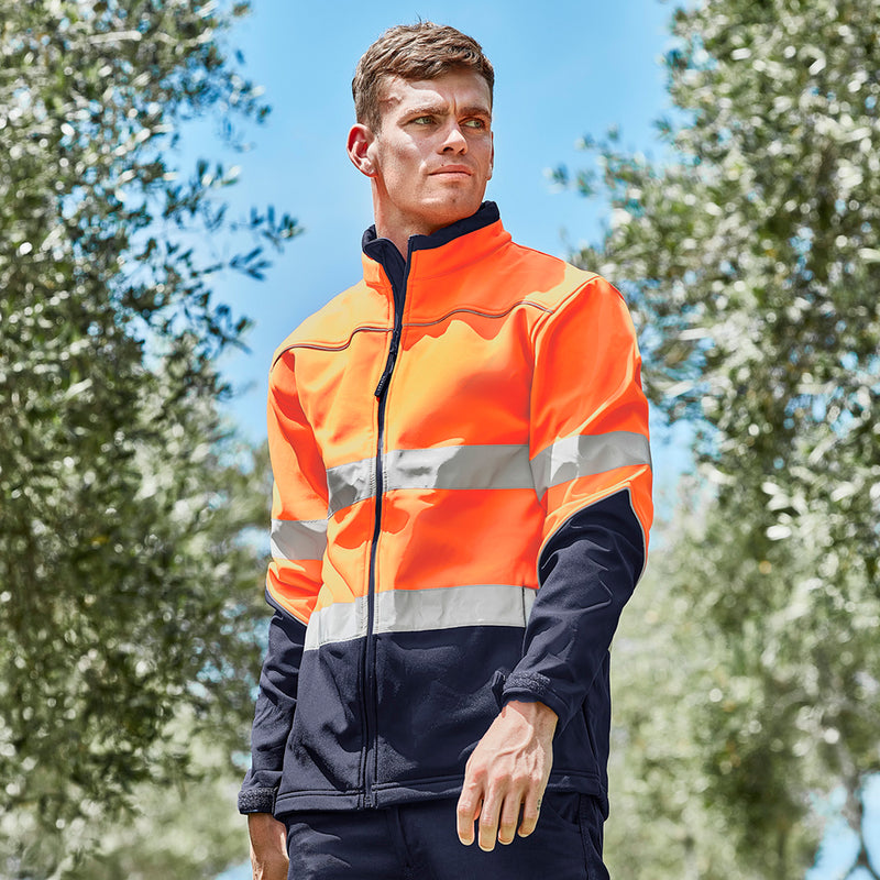 Load image into Gallery viewer, Syzmik Hi Vis Taped Soft Shell Jacket on a man outdoors, showcasing its waterproof zips, reflective piping, and adjustable cuffs, ideal for safety and visibility in active environments.
