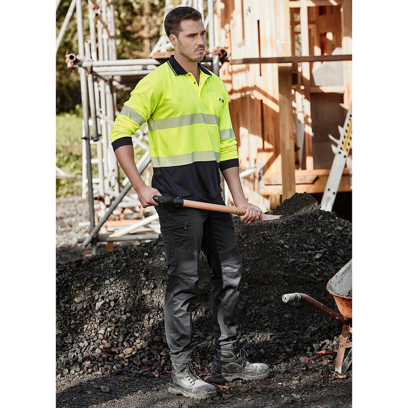 Load image into Gallery viewer, Syzmik Streetworx Stretch Pant (Non-Cuffed) worn by a man holding a shovel, showcasing its modern slim fit, unique stretch pleating, and functional pockets, ideal for active work environments.