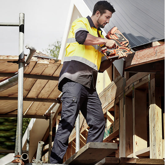 Syzmik Lightweight Drill Cargo Pant showcased on a man at a construction site, highlighting modern slim fit with reinforced knees, multiple pockets, and durable cotton drill fabric designed for safety and comfort.