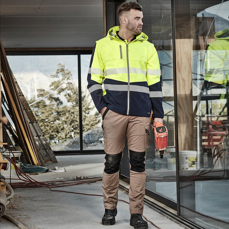Load image into Gallery viewer, Syzmik Streetworx Tough Pant worn by a man in a reflective jacket, showcasing its modern straight fit and functional pockets, including a mobile phone pocket and cargo pocket, ideal for safety work environments.
