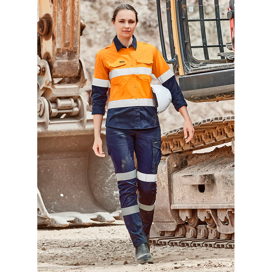 Syzmik Womens Essential Stretch Taped Cargo Pant, showcased on a construction site, features stretch reflective tape, multiple pockets, and a slim fit, highlighting comfort and safety for active work environments.