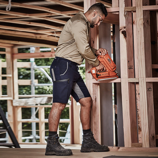 Syzmik Mens Streetworx Stretch Shorts showcased by a man holding a nail gun, highlighting the shorts' modern design and flexibility, ideal for active work environments.