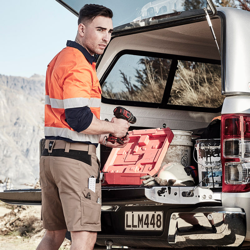 Load image into Gallery viewer, Syzmik Streetworx Tough Short showcased in an outdoor setting, worn by a man standing in a truck, emphasizing its rugged design, multiple pockets, and functional features ideal for safety and work environments.