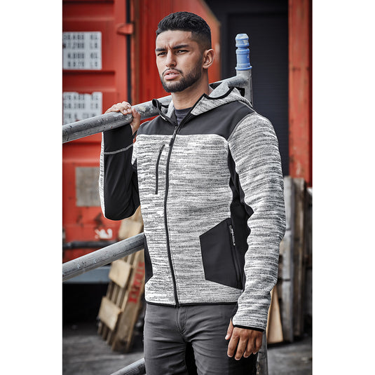 Syzmik Streetworx Knit Hoodie on a bearded man outdoors, showcasing its marle knitted fleece, reinforced soft shell panels, zip pockets, and thumb holes for built-in gloves. Ideal for active safety workwear.