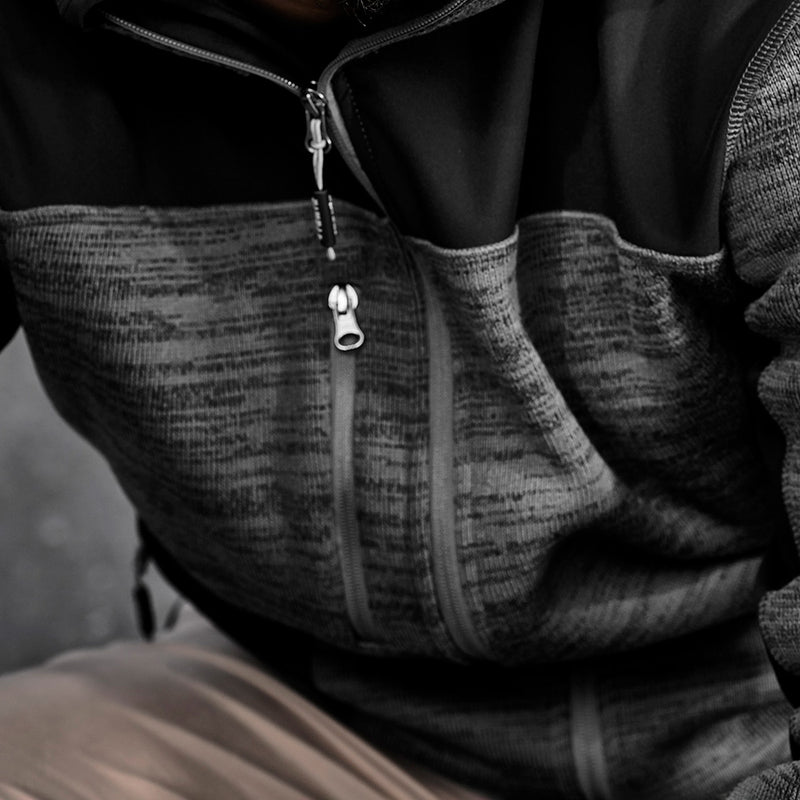 Load image into Gallery viewer, Syzmik Streetworx Knit Hoodie worn by a person indoors, showcasing its warm marle knitted fleece and reinforced soft shell panels, with visible thumb holes and chest pocket zipper for secure storage.