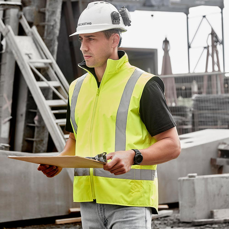 Load image into Gallery viewer, Syzmik Unisex Hi Vis Waterproof Reversible Vest worn by a construction supervisor, featuring a bright yellow high-visibility design, fleece lining, and waterproof properties, perfect for ensuring safety and comfort on-site.