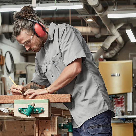 Syzmik Lightweight Tradie Work Shirt worn by a man working on wood, showcasing its functional design with triple-stitched seams, chest pockets, and underarm vents, ideal for active safety and comfort.