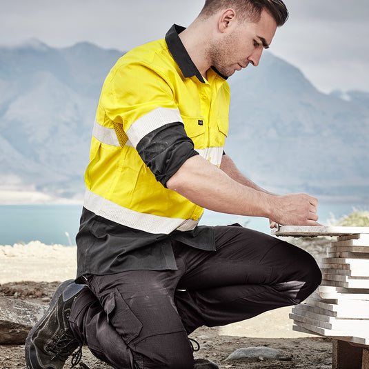 Syzmik Hi Vis Rugged Cooling Taped Spliced Shirt featuring mesh venting, reflective tape, and chest pockets, worn by a man outdoors, ideal for safety and comfort during active work environments.