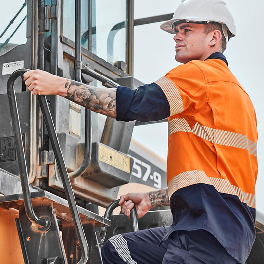 Syzmik Hi Vis Rugged Cooling Ripstop Work Shirt on a man climbing a truck; features segmented tape, mesh venting, and mechanical stretch for enhanced comfort and movement. Ideal for blue-collar workers.