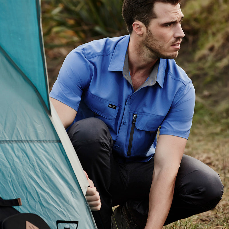 Load image into Gallery viewer, Syzmik Outdoor Ripstop Work Shirt displayed as a man squats by a tent, emphasizing its lightweight fabric, breathable mesh, and practical chest pockets, ideal for active outdoor work settings.