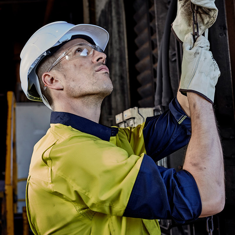 Load image into Gallery viewer, Syzmik Hi Vis Closed Front L/S Work Shirt featuring a man in a hard hat and gloves, highlighting the shirt's mesh vent inserts and chest pockets, ideal for safety-focused work environments.