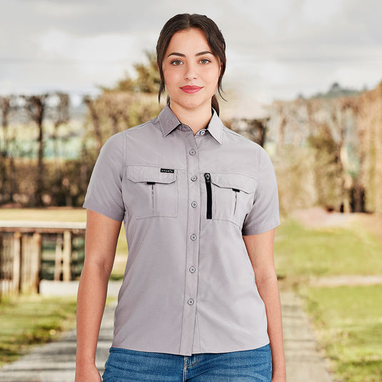 Syzmik Womens Outdoor Short Sleeve Shirt featuring lightweight, breathable 100 GSM polyester with underarm mesh and back venting, crinkle-resistant fabric, two chest pockets, and a mobile phone zip pocket for versatile outdoor wear.
