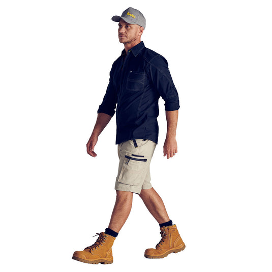 The Bisley Flex & Move Stretch Utility Zip Cargo Short features light-tan multi-pocket design with durable Cordura® accents, ideal for active workwear. Paired with a dark shirt and sturdy work boots.