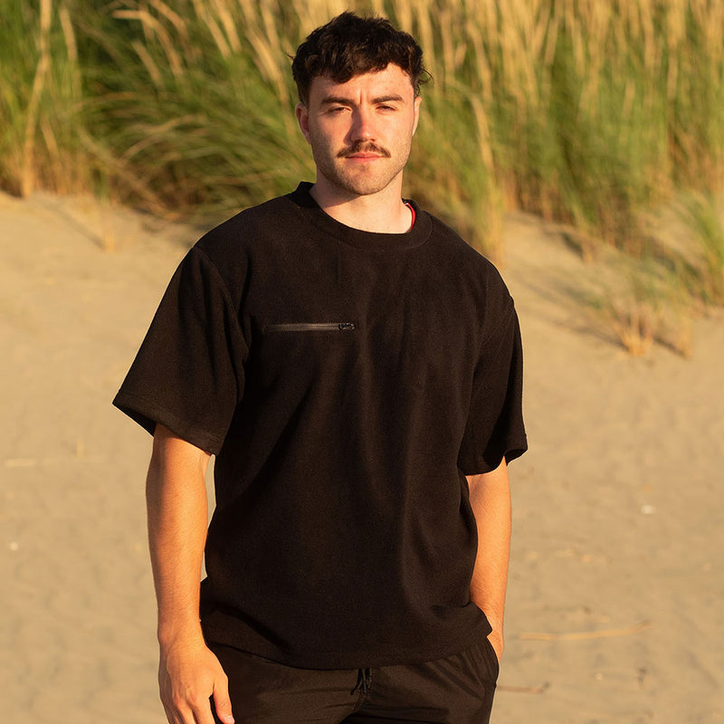 Load image into Gallery viewer, Close-up of a man wearing the Monowai Fleece Tee, showcasing the zippered chest pocket and side seams. Ideal for outdoor work, this tee offers durability and comfort with its breathable, recycled polyester fabric.
