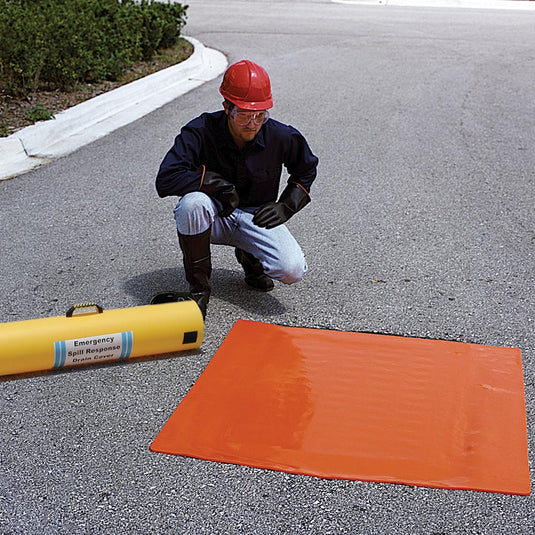 Worker in safety gear demonstrates the Ultra Drain Seal Orange 91 x 91cm, sealing a storm drain with its flexible, urethane construction. The product's yellow storage tube is visible beside him.