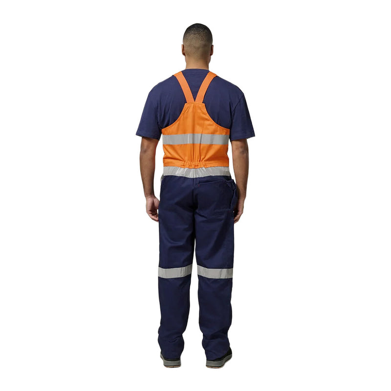 Load image into Gallery viewer, Person wearing Hard Yakka Easy Action Hi Vis Cotton Bib Overall with reflective stripes, featuring reinforced pockets and elastic straps, suited for construction work, promoting safety and visibility on industrial sites.
